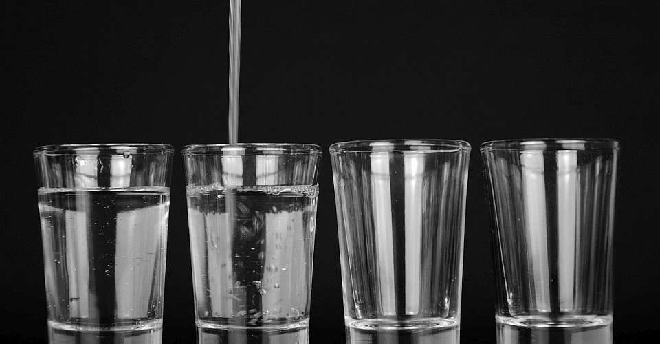 Four glasses in the process of being filled with water from a water dispenser. Each glass is being filled with the same amount of water, illustrating that God loves all believers equally and wants to give each of them his Holy Sprit fully.